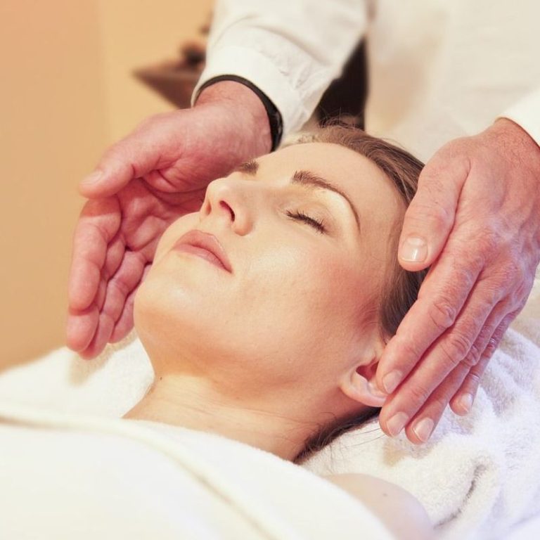 Frau entspannt sich während einer Massage mit Händen, die ihren Kopf berühren.